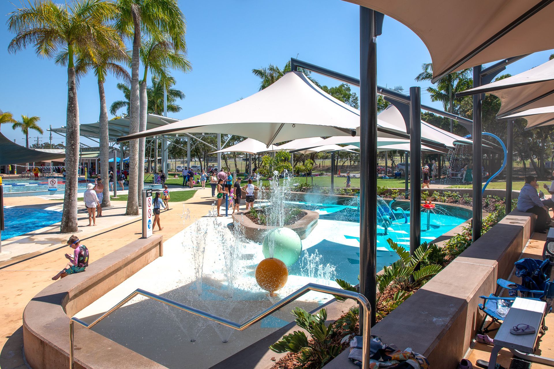 Poolside resort with palm trees, white shade sails, and a water feature beside a lounge area — C & A Concreting In Craignish, QLD