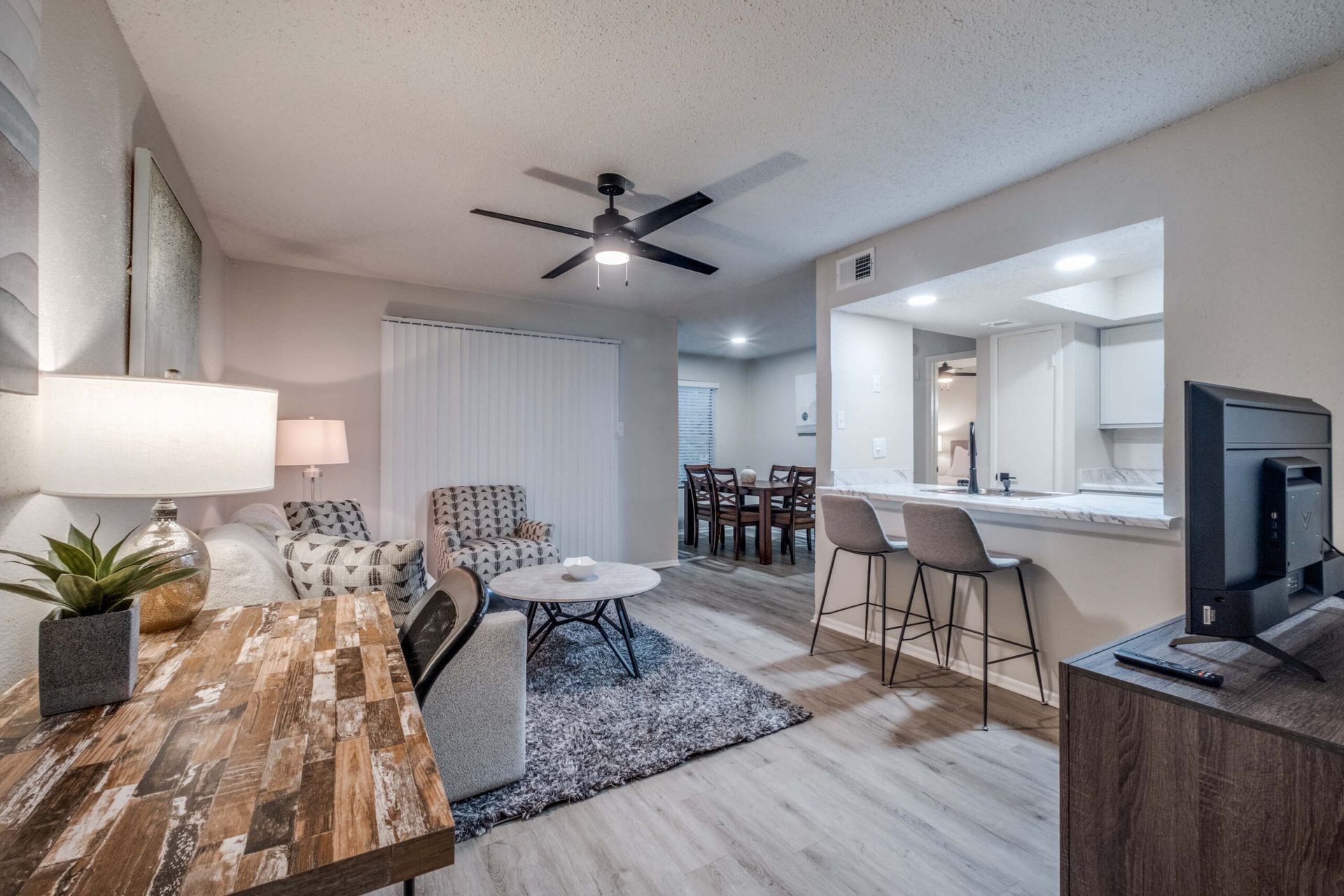 Bright open-plan living room with sofa, coffee table, TV, dining area, and kitchen pass-through