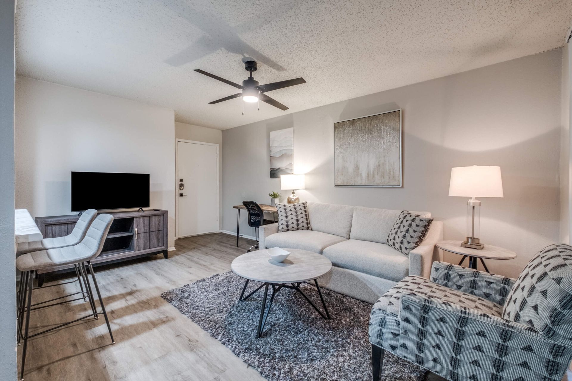 Modern living room with gray sofa, patterned chairs, TV, ceiling fan, and round coffee table
