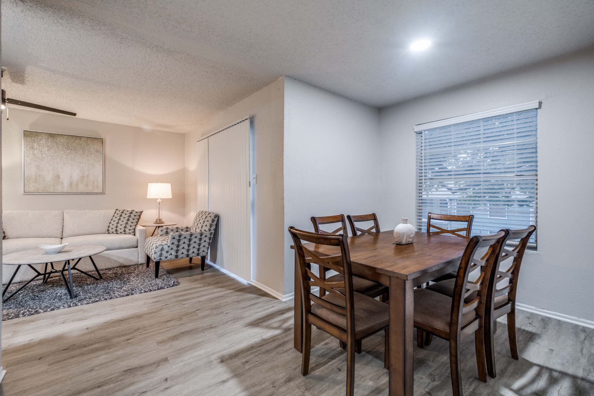 Open living-dining room with white sofa, wood dining table, lamp, and window blinds