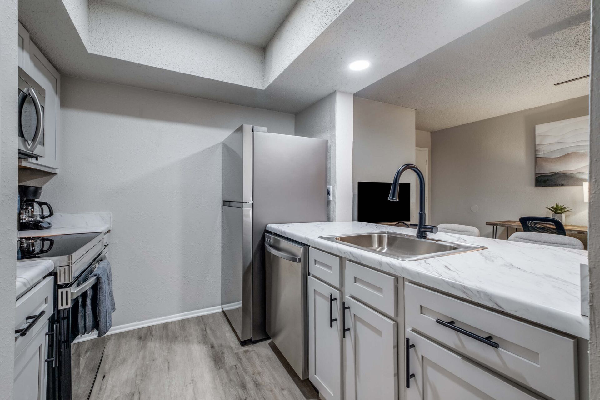 Modern white kitchen with stainless steel appliances, island sink, and gray wood flooring