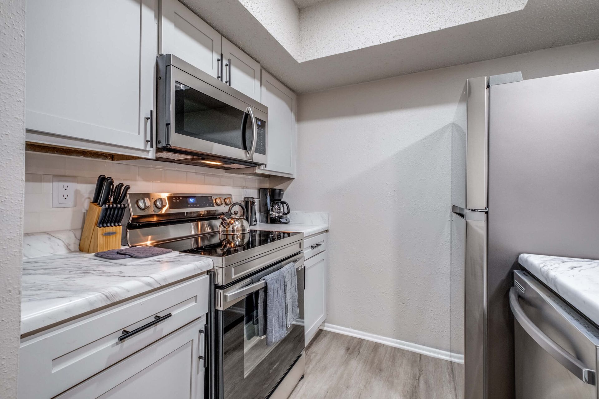 Modern kitchen with white cabinets, stainless steel appliances, and a stove with utensils on the counter