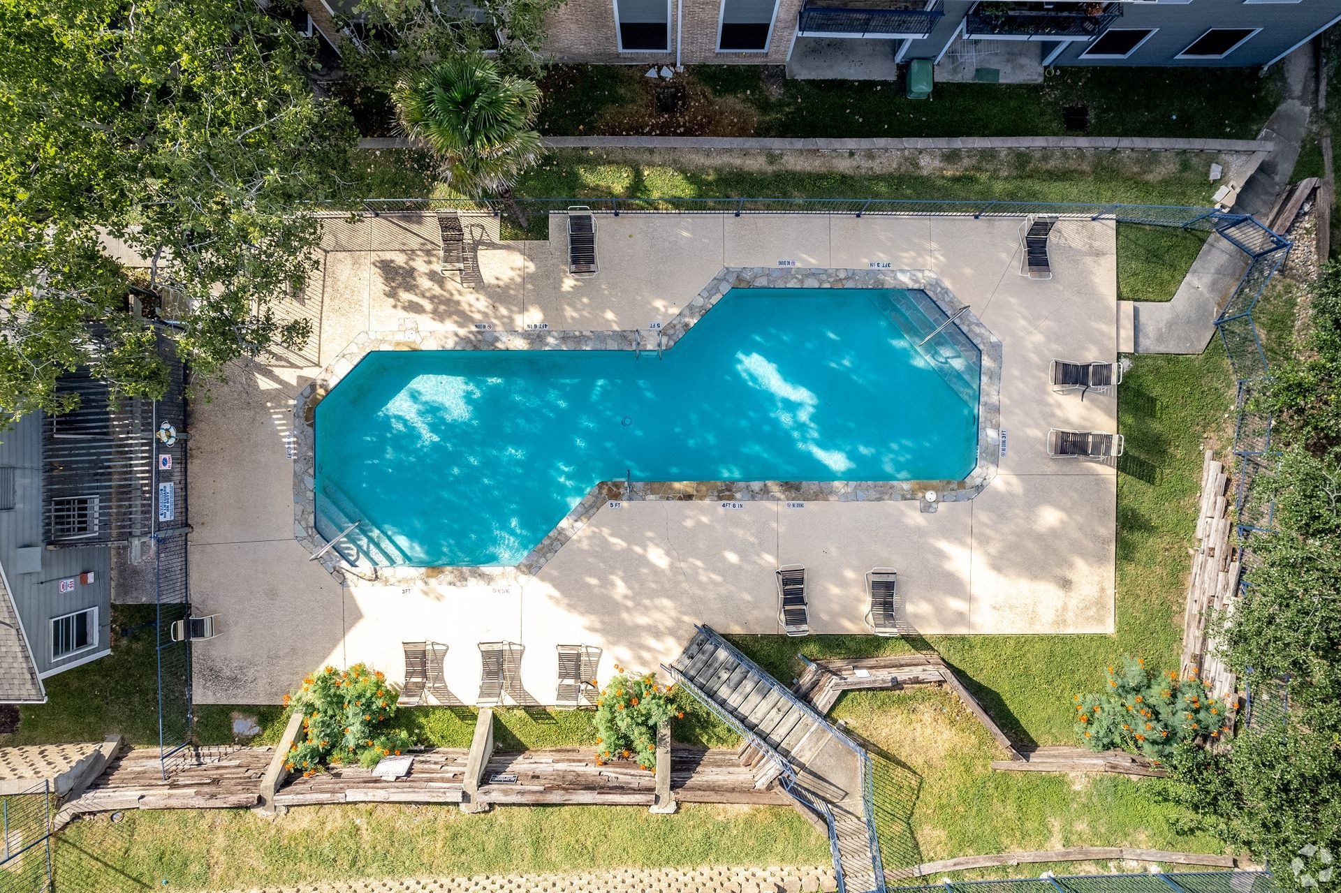Aerial view of a turquoise swimming pool beside a building and landscaped courtyard