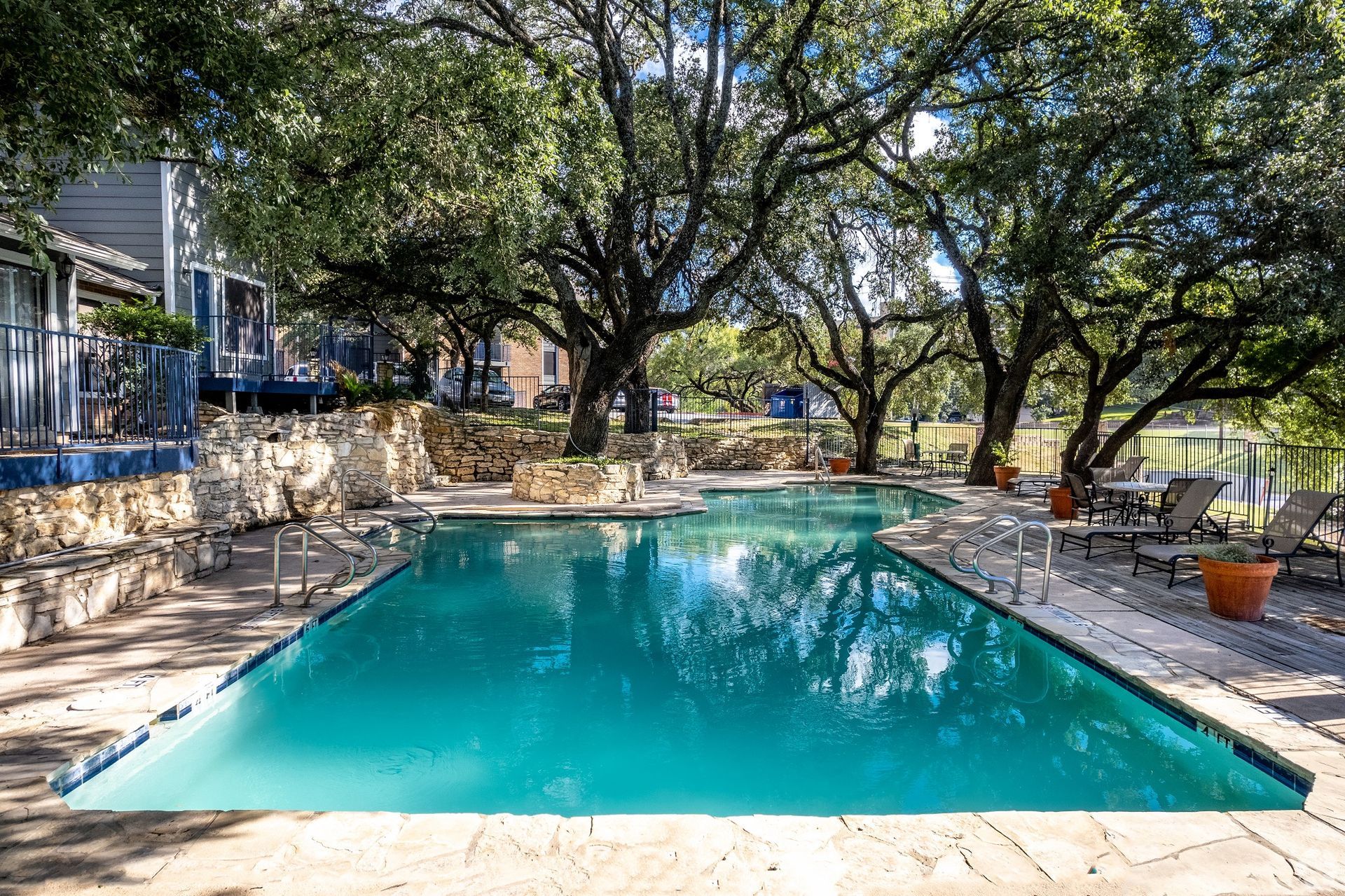 Backyard swimming pool shaded by large trees, with stone patio and house steps nearby