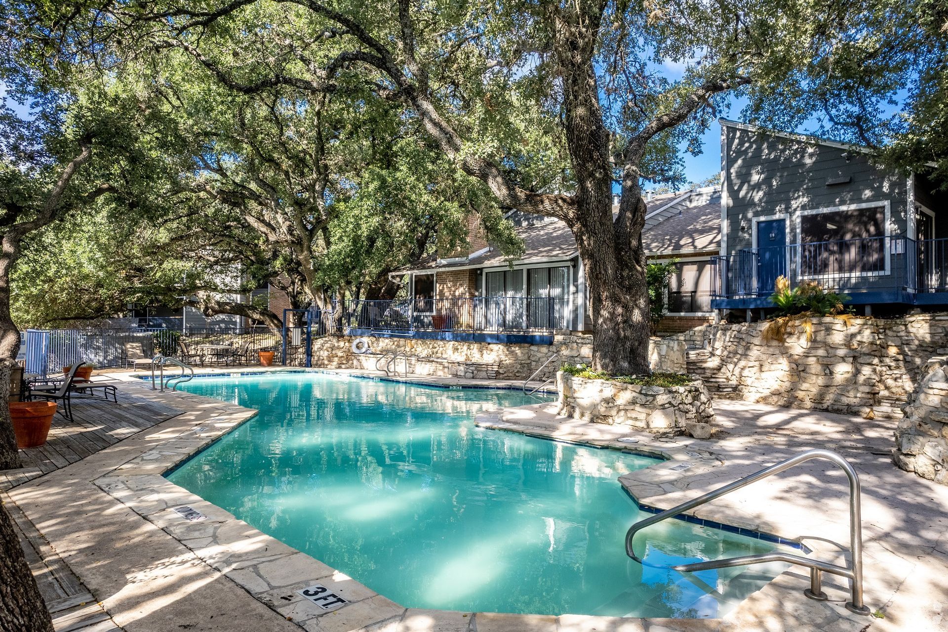 Backyard swimming pool under shaded trees beside a stone patio and house