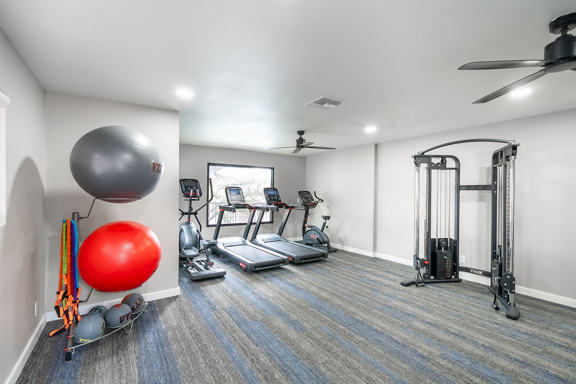 Modern home gym with treadmills, cable machine, exercise balls, and resistance bands on carpet.