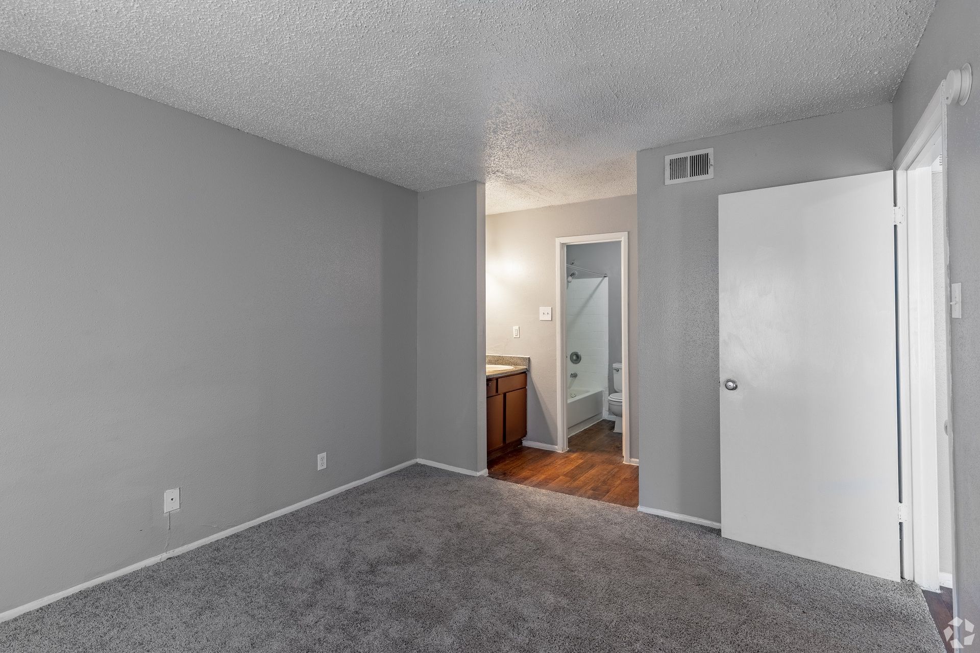 Empty gray bedroom with carpet, open closet door, and doorway to a bathroom or hall.