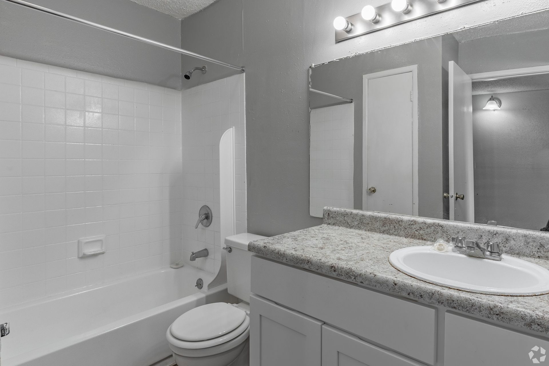 Bright bathroom with a white tub, toilet, granite vanity, and large mirror.