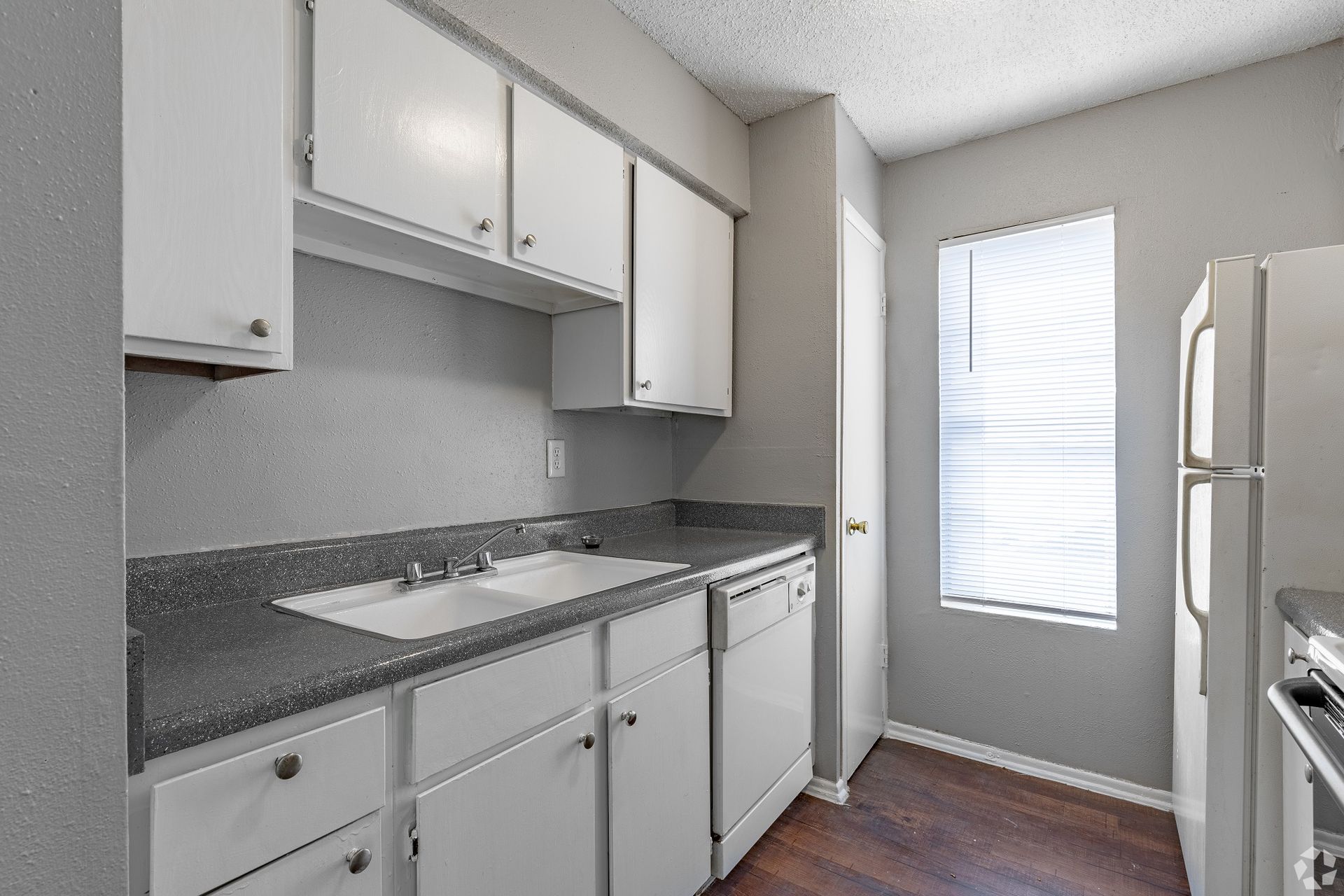 Compact galley kitchen with white cabinets, gray countertop, and a window by the refrigerator.