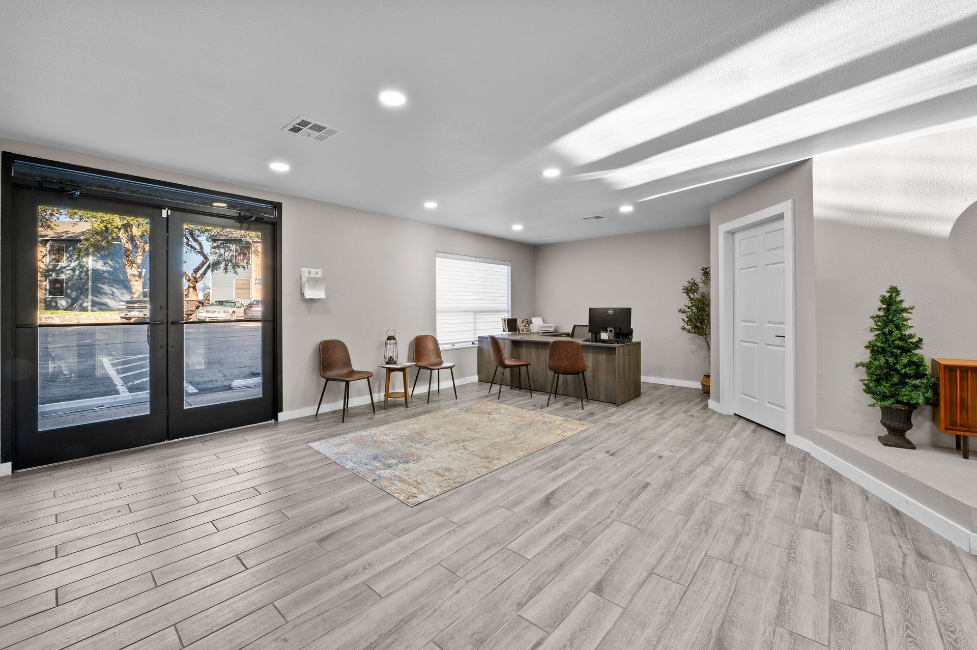 Bright modern living room with gray floors, large windows, desk, chairs, and a Christmas tree