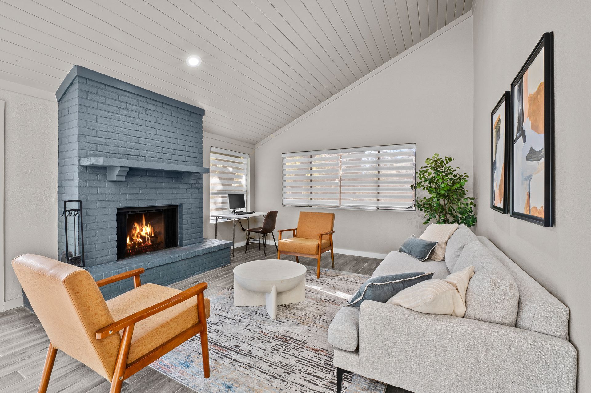 Cozy living room with blue fireplace, gray sofa, tan chairs, and large windows