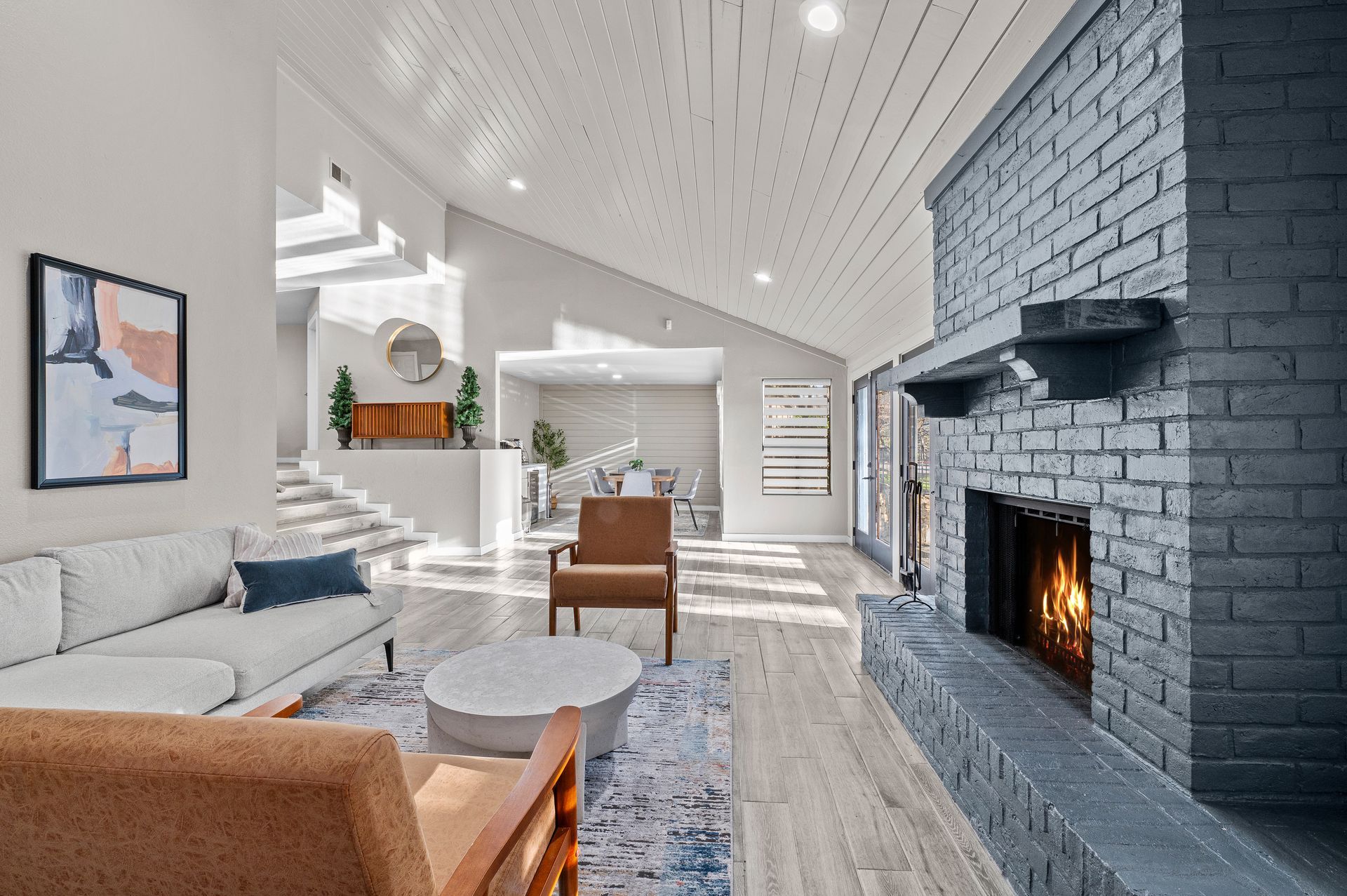 Bright modern living room with white sofa, tan chair, gray rug, and a lit black brick fireplace