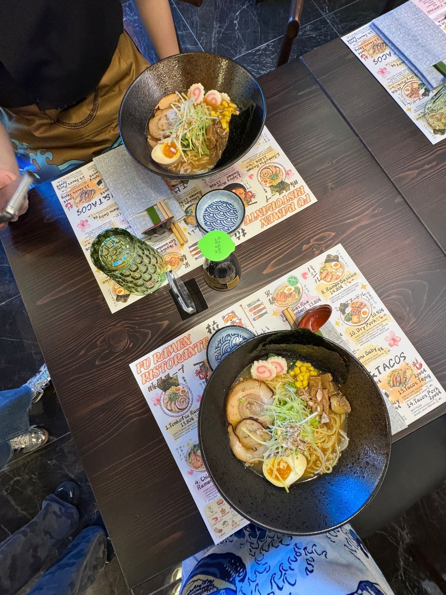 Vista dall'alto di due ciotole di ramen su un tavolo di ristorante, con menù e bacchette.
