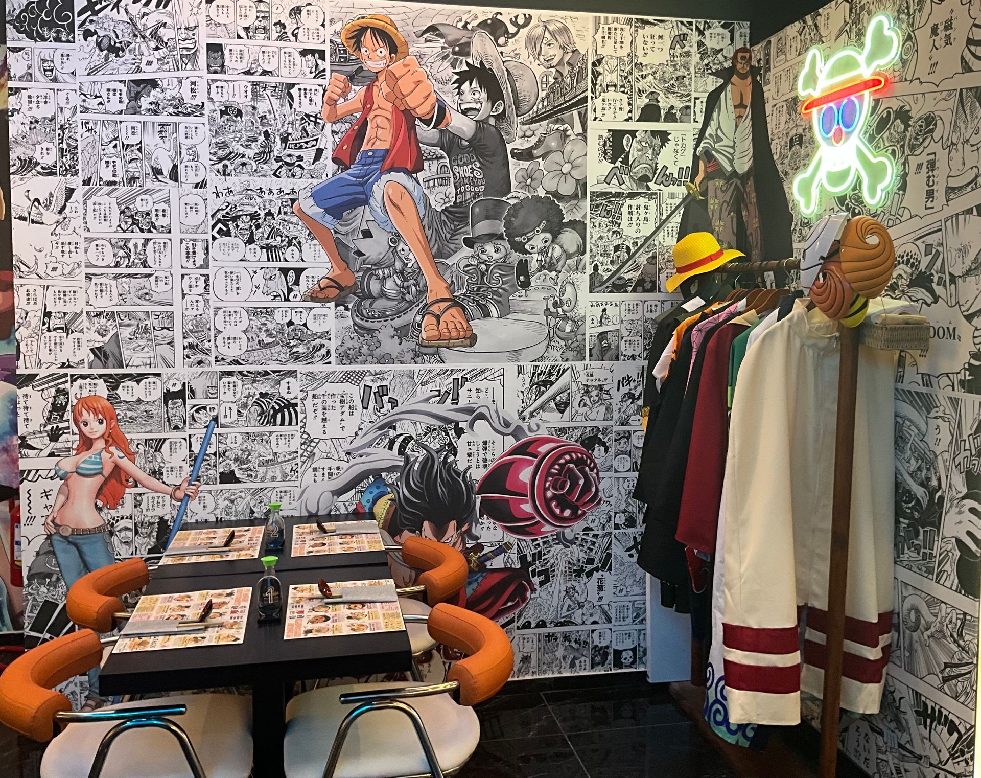 Angolo caffè a tema fumetti con decorazioni murali, tavolino, sedie arancioni e appendiabiti sotto luci al neon.