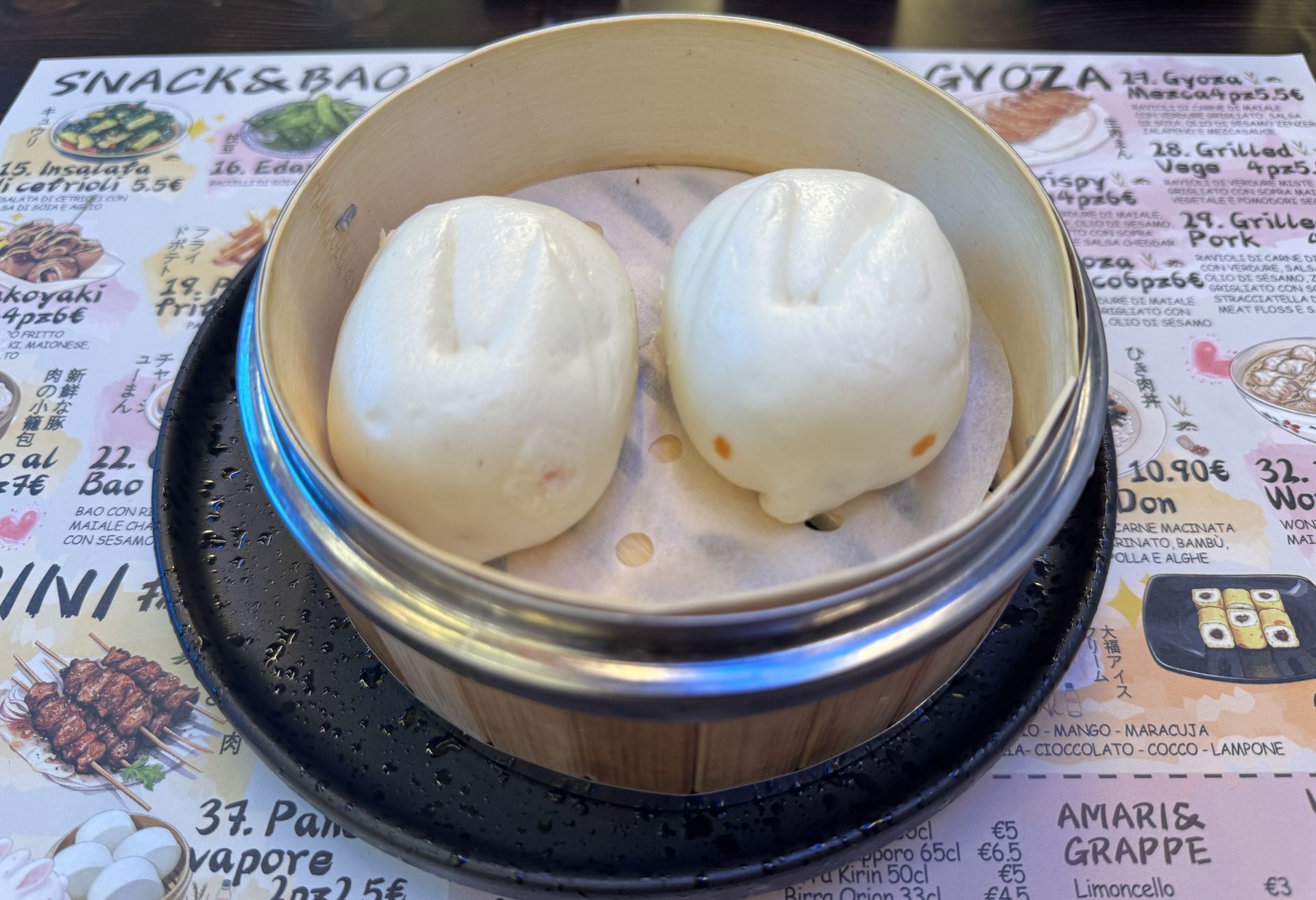 Due panini bianchi al vapore in un cestino di bambù su un tavolo del menù.