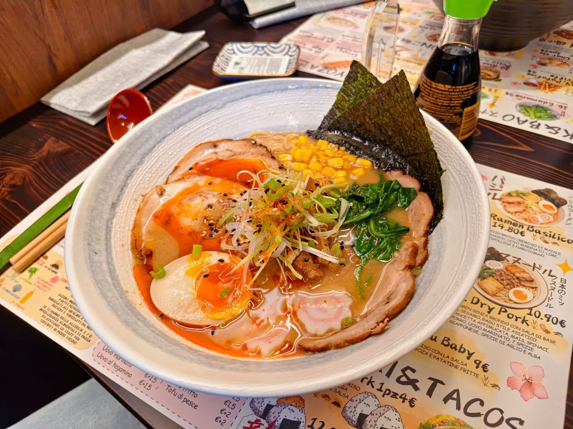 Una ciotola di noodles con uovo, maiale, alghe ed erbe aromatiche su un tavolo di ristorante.