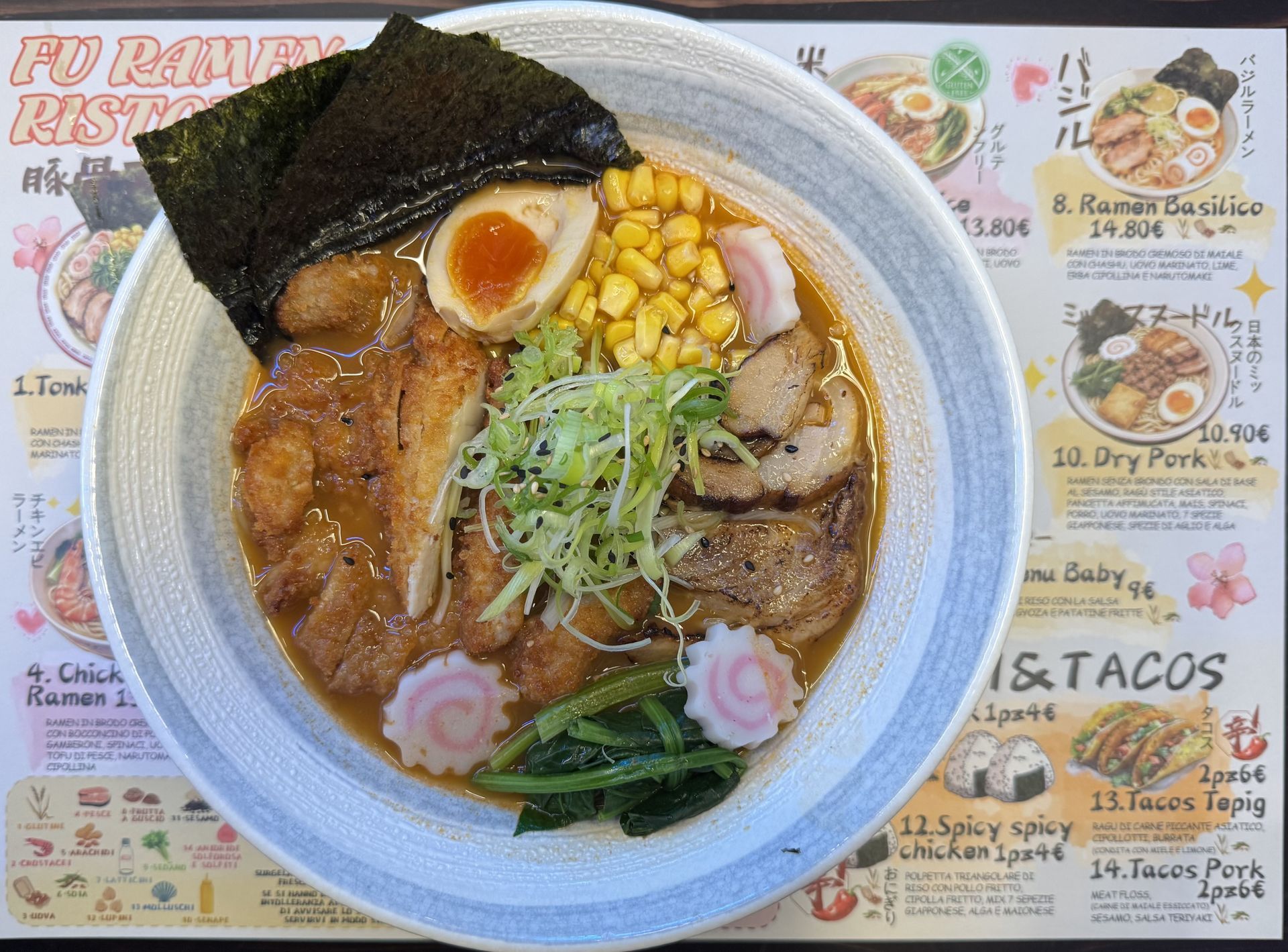 Una ciotola di ramen con maiale, uovo, mais, verdure e alghe su un tavolo del menù.