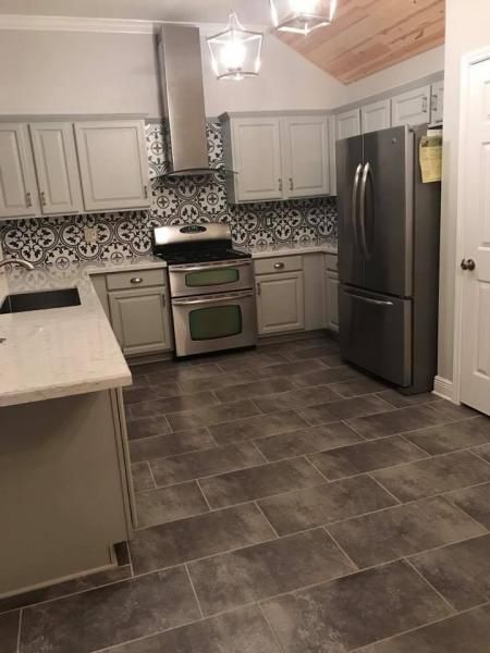 Modern kitchen with white cabinets, gray tile floor, stainless steel stove and refrigerator, and mosaic backsplash