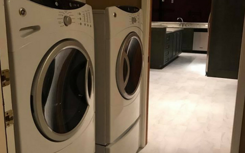 Two beige front-loading washing machines in a laundry room with white tile flooring.