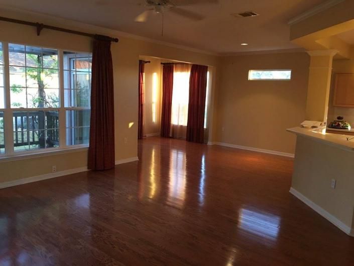 Empty living room with hardwood floors, large windows, and warm sunlight from the sliding glass door