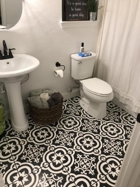 Small bathroom with black-and-white patterned floor, white pedestal sink, toilet, and basket beside a shower curtain.