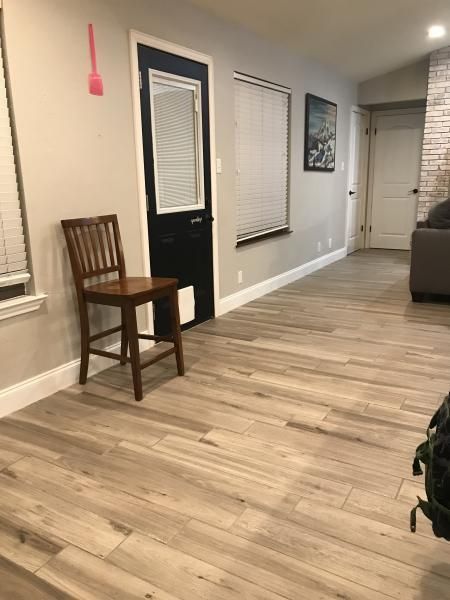 Empty living room with wood floors, a chair by the wall, windows with blinds, and a couch at the right edge