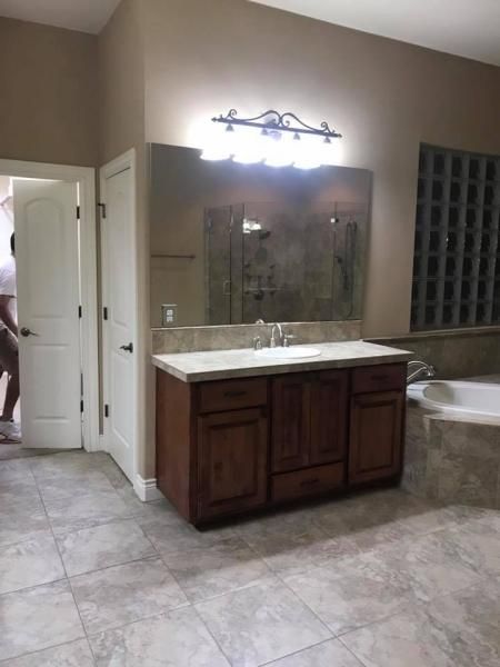 Bathroom with double vanity, wall mirror and light, gray tile floor, and a tub beside glass block windows.