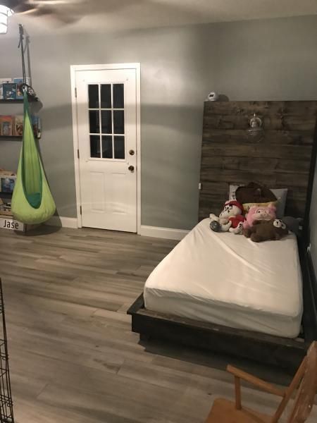 Minimalist bedroom with gray walls, white door, bed with stuffed animals, and green hanging chair
