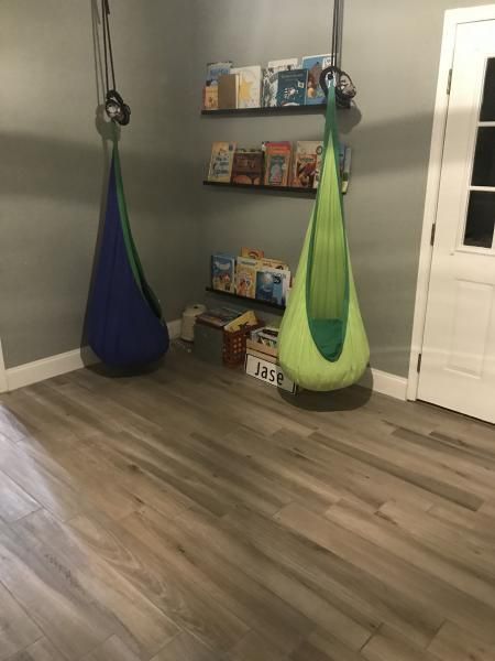 Living room with two hanging pod chairs, a shelf of board games, and a doorway on the right.