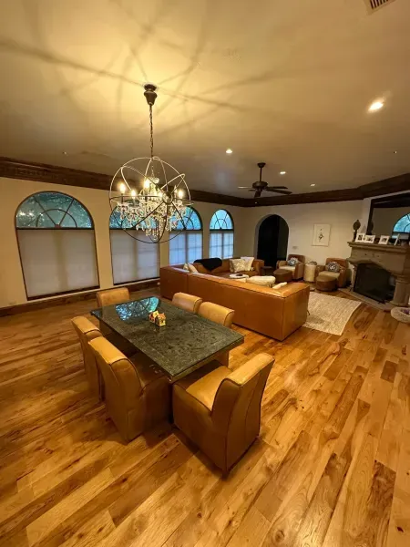 Modern living room with hardwood floors, tan sofas, glass dining table, chandelier, and arched windows