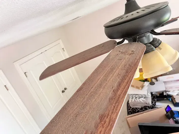 Close-up of a brown ceiling fan with dust-covered blades in a room with a white door.