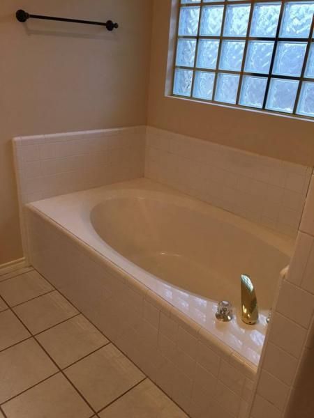 Empty white bathtub in a tiled bathroom with a glass block window and towel bar