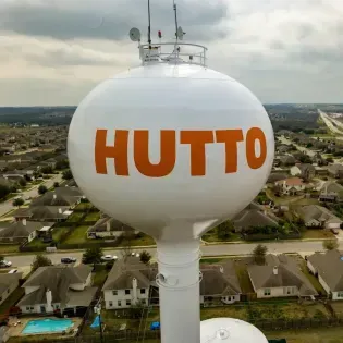 White Hutto water tower above a suburban neighborhood, with orange “HUTTO” lettering.