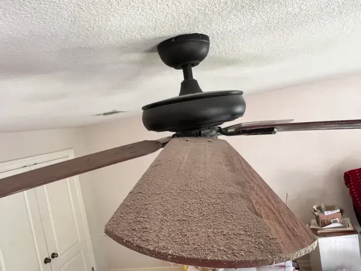 Close-up of a ceiling fan with a tan lampshade attached, in a white room.