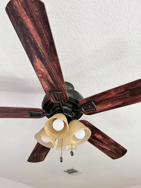 Ceiling fan with five dark wood blades and four beige light shades on a white ceiling