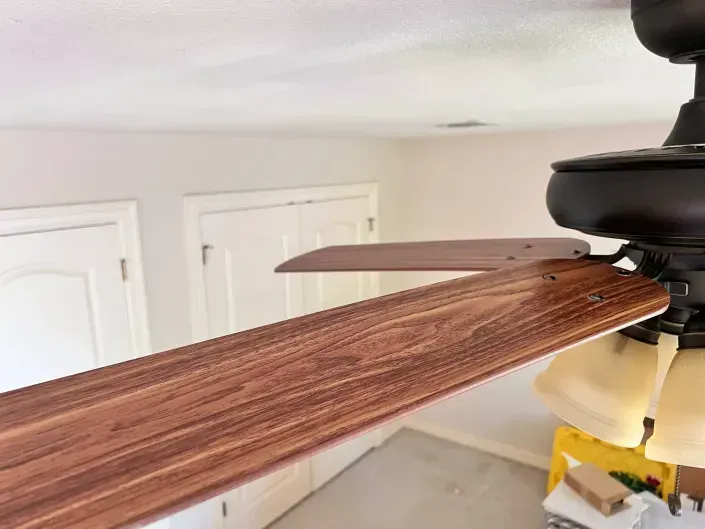 Wood-look ceiling fan blade being installed in a white room