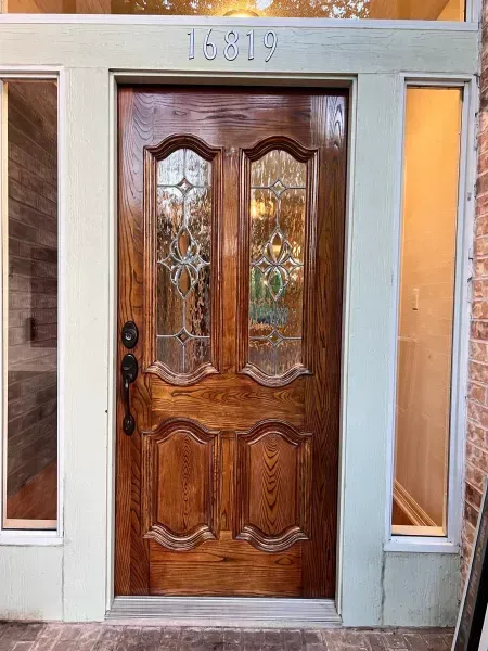 Wooden front door with decorative glass panels, framed by light stone and narrow side windows.