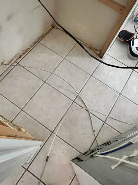 Small tiled floor corner with loose cables and a gray appliance or heater on the right