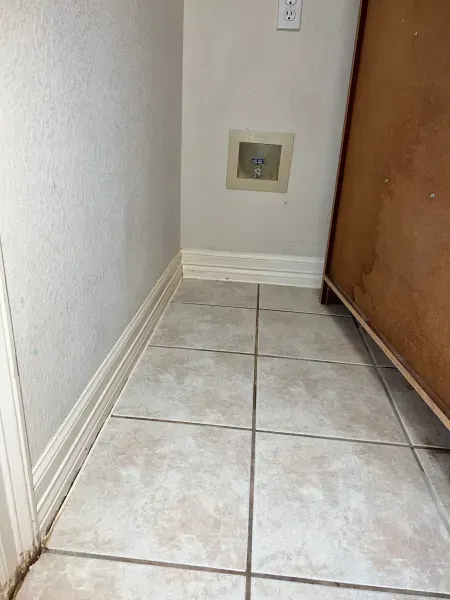 Narrow tiled hallway corner with white walls, baseboards, and a wooden door.