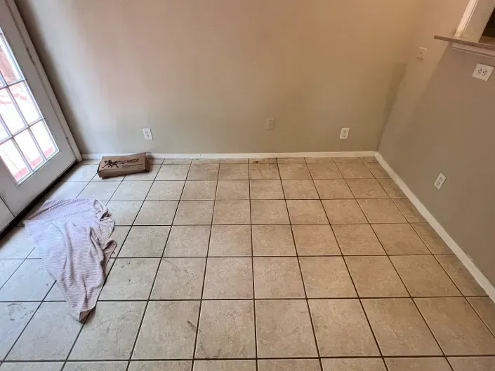 Empty room with beige walls, tiled floor, and a door with light from windows on the left.