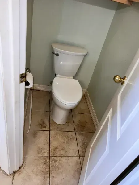 Small beige-tiled bathroom with a white toilet in a narrow alcove, viewed through an open door.
