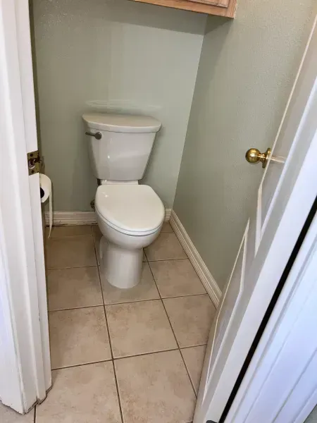 Small bathroom with a white toilet, beige tile floor, and pale green walls.
