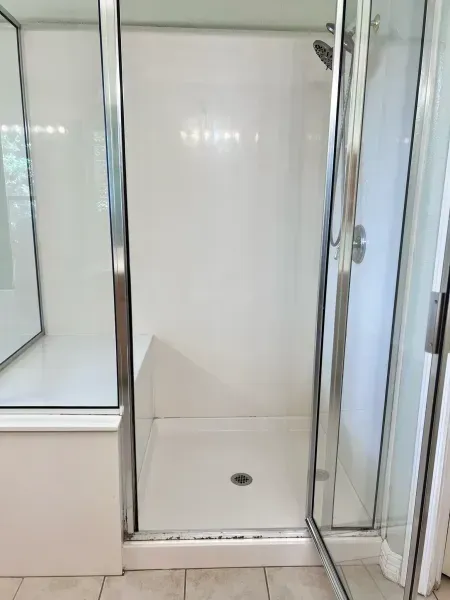 Shower stall with glass doors, white walls, and a built-in bench over a tiled floor.