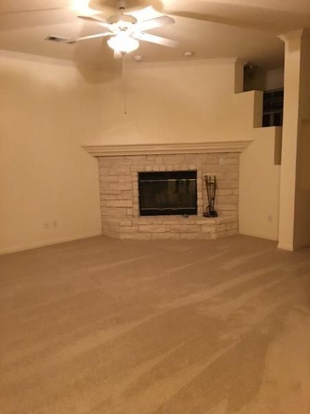 Empty living room with beige carpet, fireplace, and ceiling fan under warm lighting
