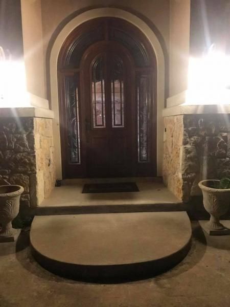 Front entrance with arched wooden double doors, stone walls, and warm exterior lights at night