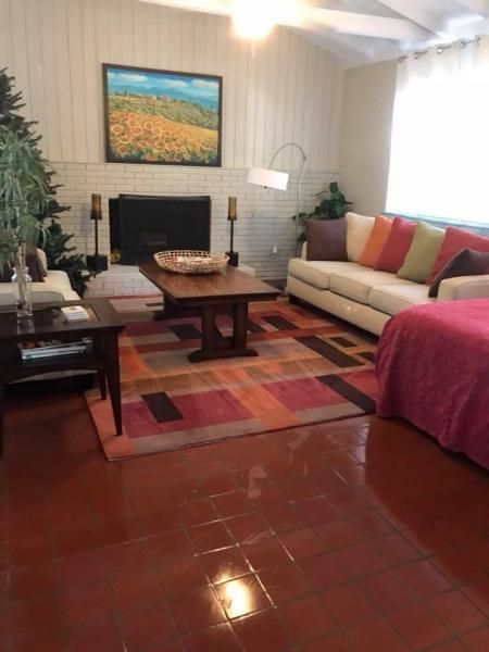 Living room with beige sofa, coffee table, rug, lamp, wall art, and glossy red tile floor.