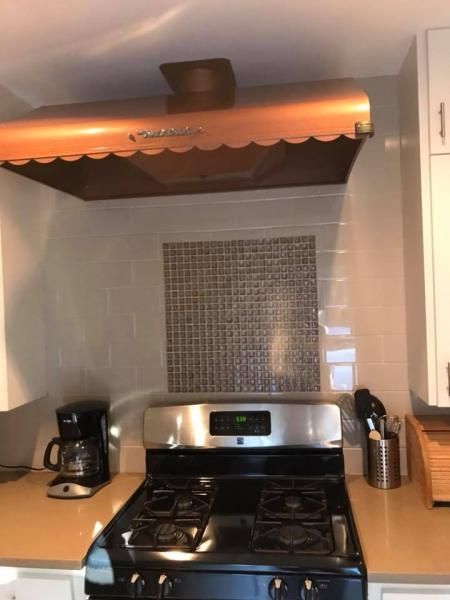Kitchen stove with stainless range hood, tiled backsplash, and coffee maker on wooden counters.