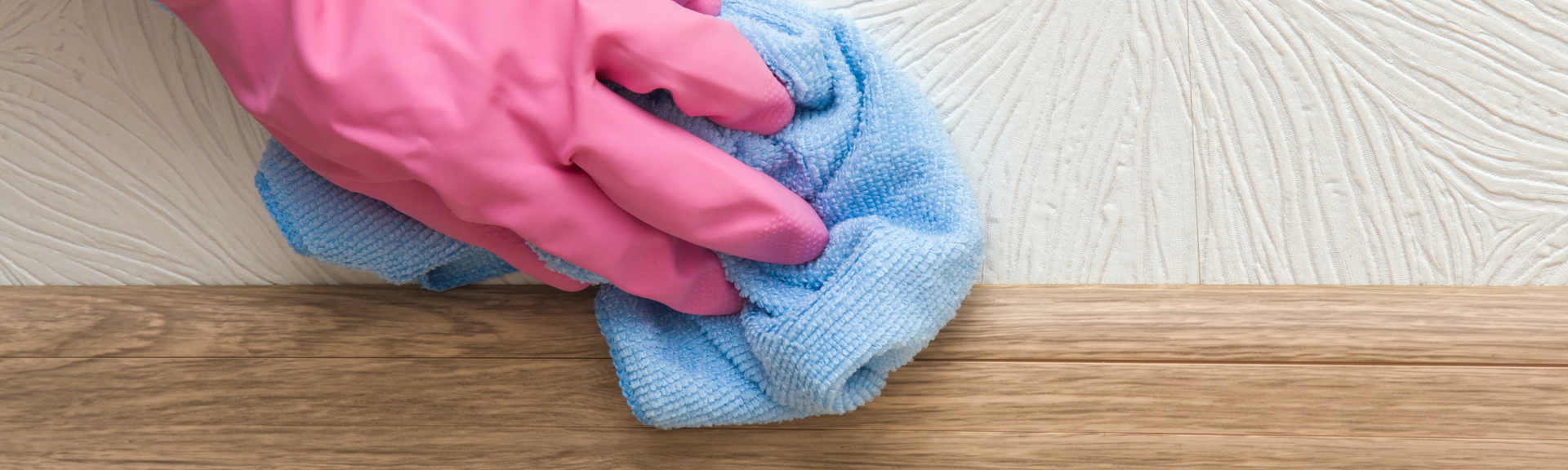 Pink-gloved hand wiping a wooden floor with a blue cloth