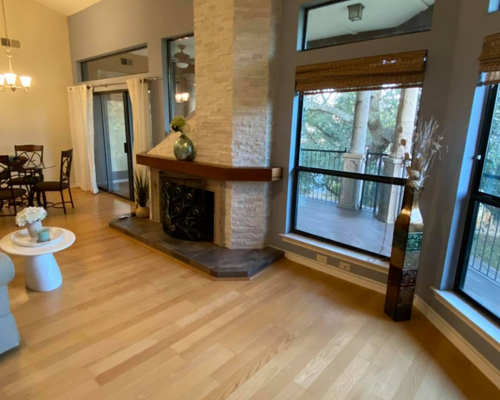 Bright living room with wood floor, corner fireplace, large windows, and a balcony view