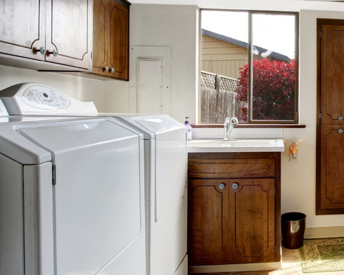 Laundry room with white washer, wooden cabinets, sink, and window overlooking a garden